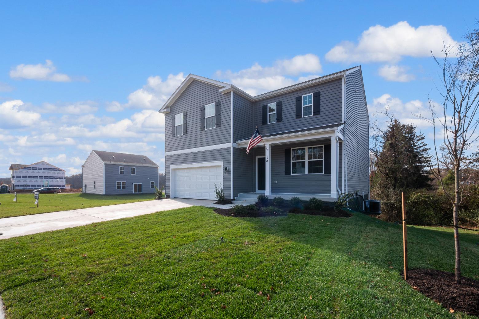 Side view of Two-Story Galen plan home with vertical plank siding, two-car garage, and covered porch with an American Flag