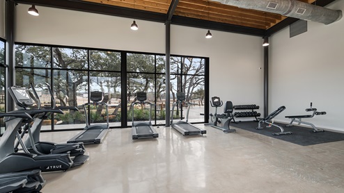 Bulverde Texas DR Horton Homes Copper Canyon New Construction Homes indoor fitness center with stained concrete flooring treadmills ellipticals stationary bike rack free weights stationary weight machines and floor to ceiling windows for plenty of natural lighting