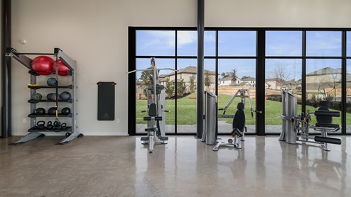 Bulverde Texas DR Horton Homes Copper Canyon New Construction Homes indoor fitness center with stained concrete flooring rack medicine balls kettlebells stationary weight machines and floor to ceiling windows for plenty of natural lighting