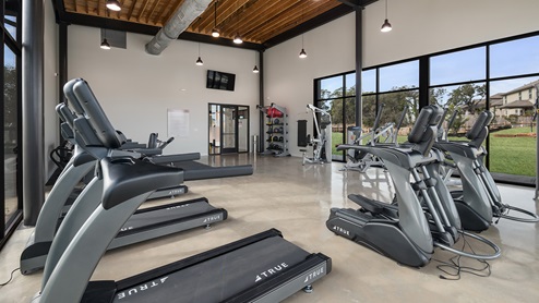 Bulverde Texas DR Horton Homes Copper Canyon New Construction Homes indoor fitness center with stained concrete flooring treadmills ellipticals full body weight machines rack of free weights and floor to ceiling windows for plenty of natural lighting
