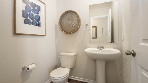 San Antonio Texas Express Homes DR Horton Applewood Model Home Jasmine floor plan 2182 square feet New Construction Homes powder or half bathroom with hard surface flooring toilet pedestal sink mounted wall mirror wicker basket wall decor framed wall art