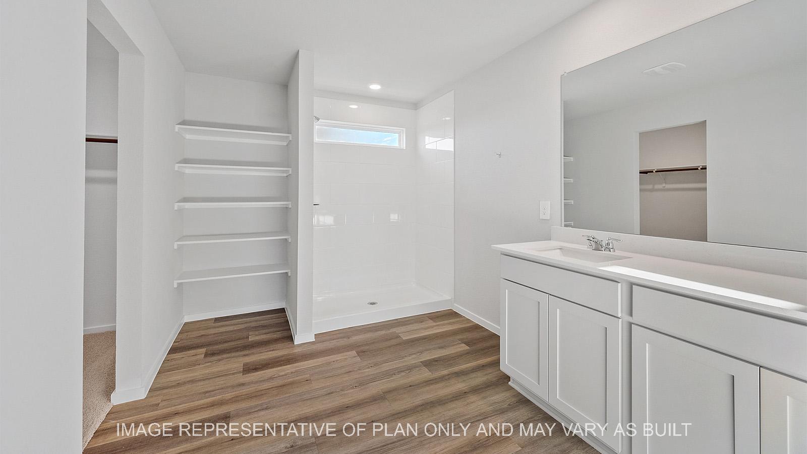 Emma primary bathroom with built-in shelving, quartz vanity countertop, vinyl plank flooring, and white ceramic tile shower surround.