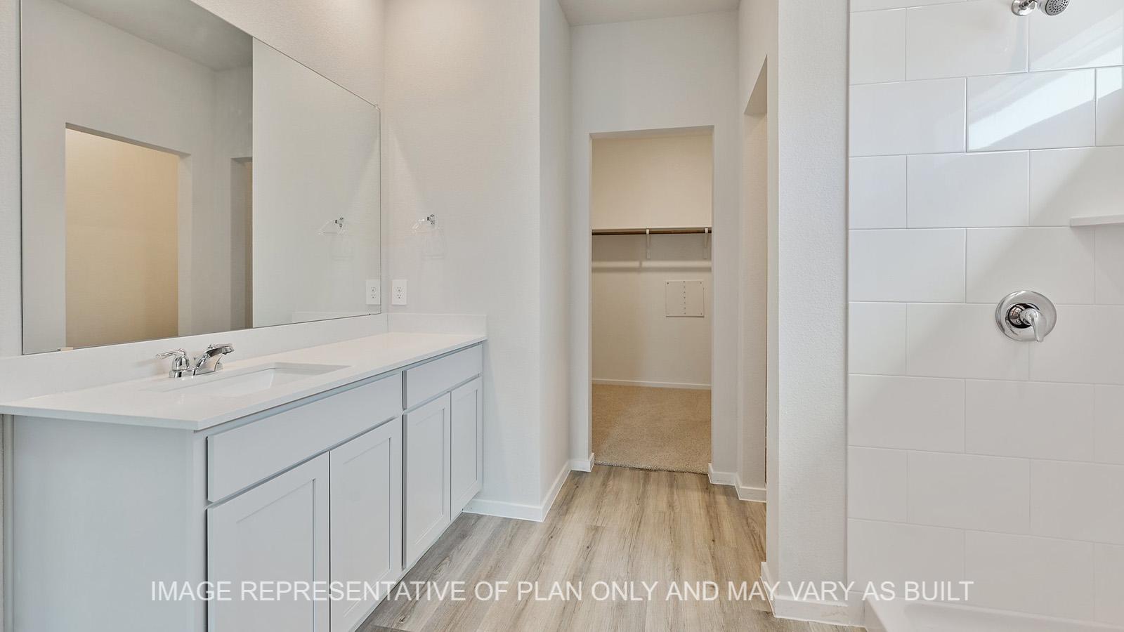 Jasmine primary bathroom with white cabinetry, granite countertops, ceramic tile shower surround, closet access and vinyl plank flooring.