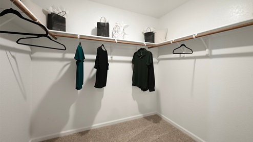 Pleasant Hill Model Home primary closet with carpeted flooring and clothes hanging.
