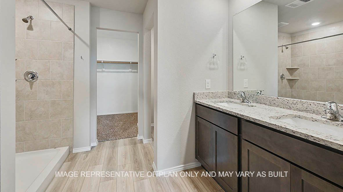 Fargo primary bathroom with dark stained cabinetry, granite countertops, ceramic tile shower surround, vinyl plank flooring and view to closet.