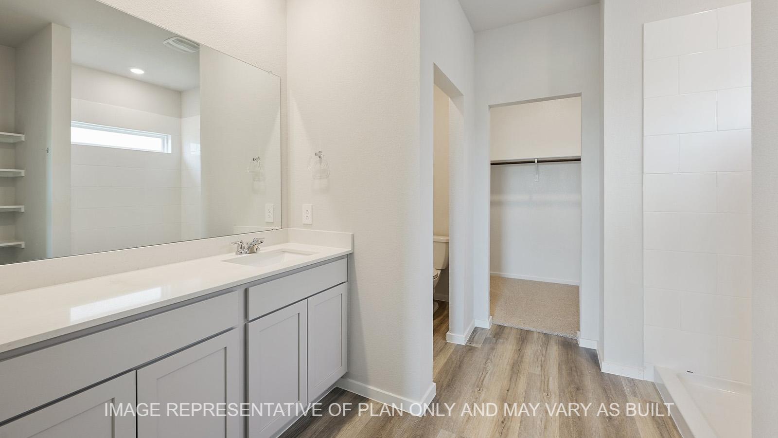 Midland primary bathroom with gray cabinetry, granite countertops, linen shelving, ceramic tile shower surround, and vinyl plank flooring.