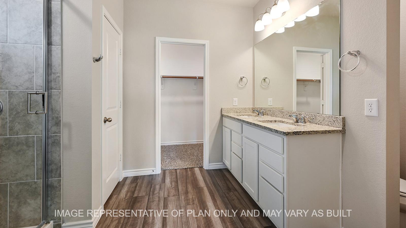 Alpine primary bathroom with white cabinetry, vinyl plank flooring, granite countertops, ceramic tile shower surround, and closet entry.