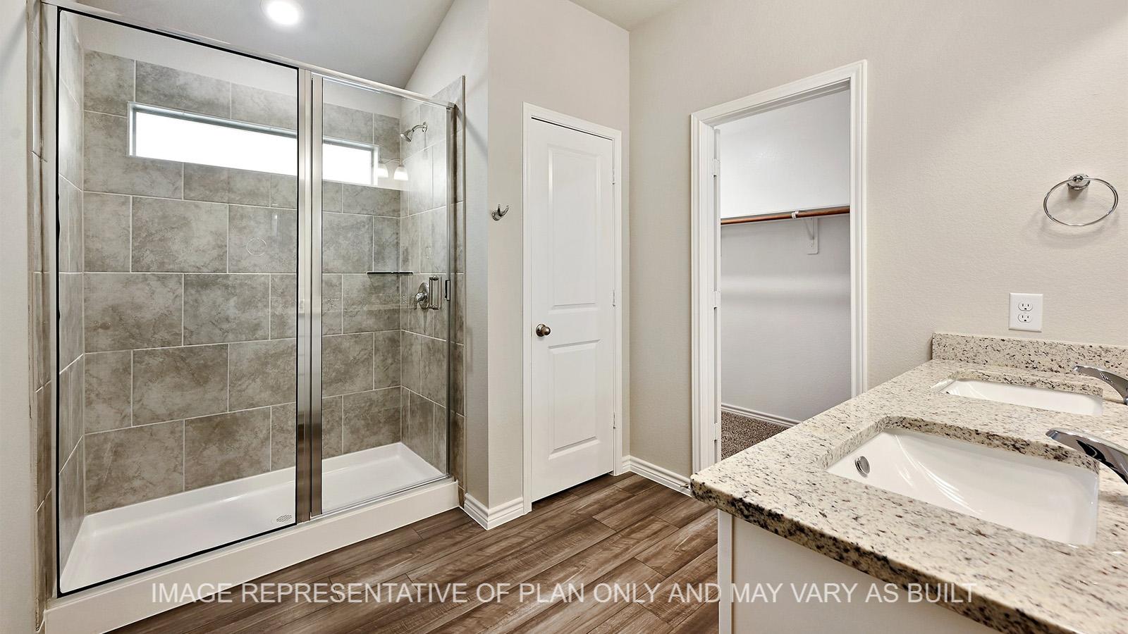Alpine primary bathroom with white cabinetry, vinyl plank flooring, granite countertops, ceramic tile shower surround, and closet entry.