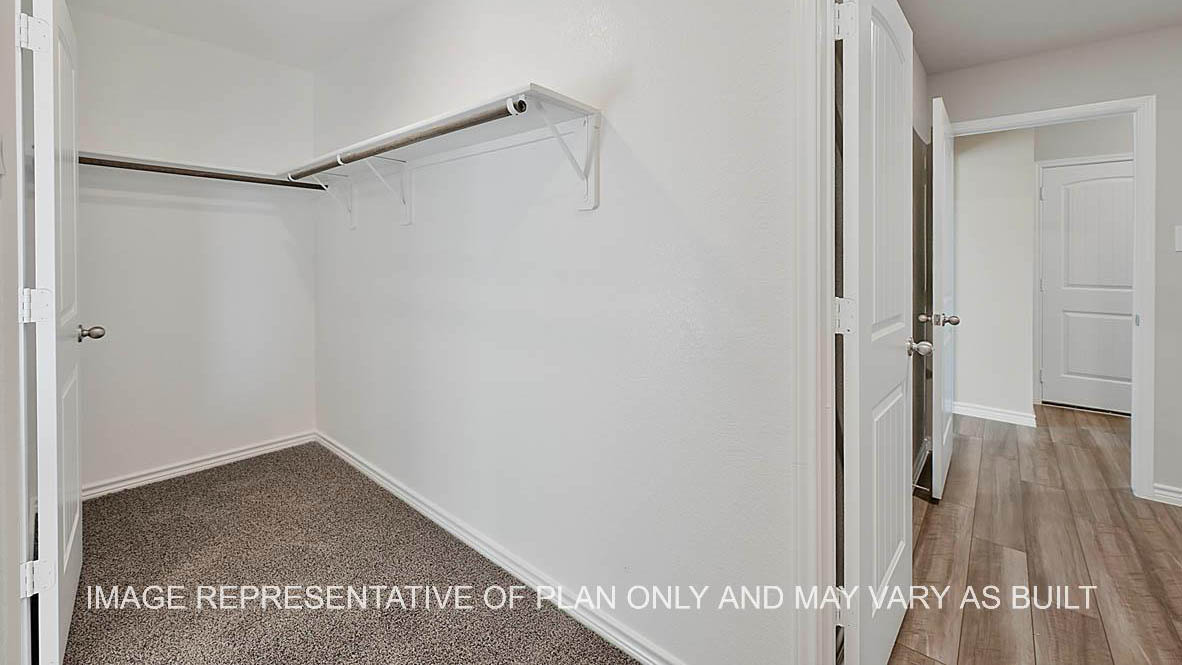 Prescott primary walk-in closet with carpet flooring and view to utility room.