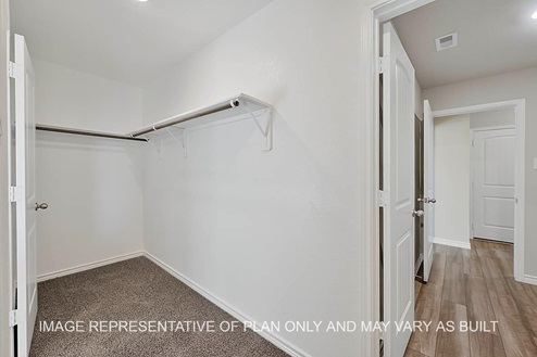 Prescott primary walk-in closet with carpet flooring and view to utility room.