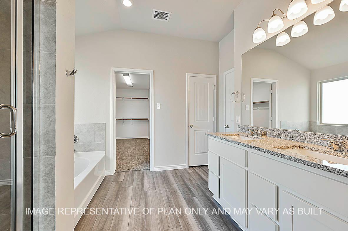 Kiawa primary bathroom with granite countertops, white cabinets, ceramic tile shower and tub surround, vinyl plank flooring, and view to closet.
