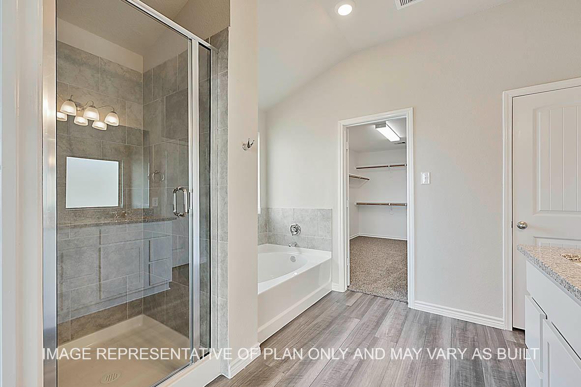 Kiawa primary bathroom with granite countertops, white cabinets, ceramic tile shower and tub surround, vinyl plank flooring, and view to closet.