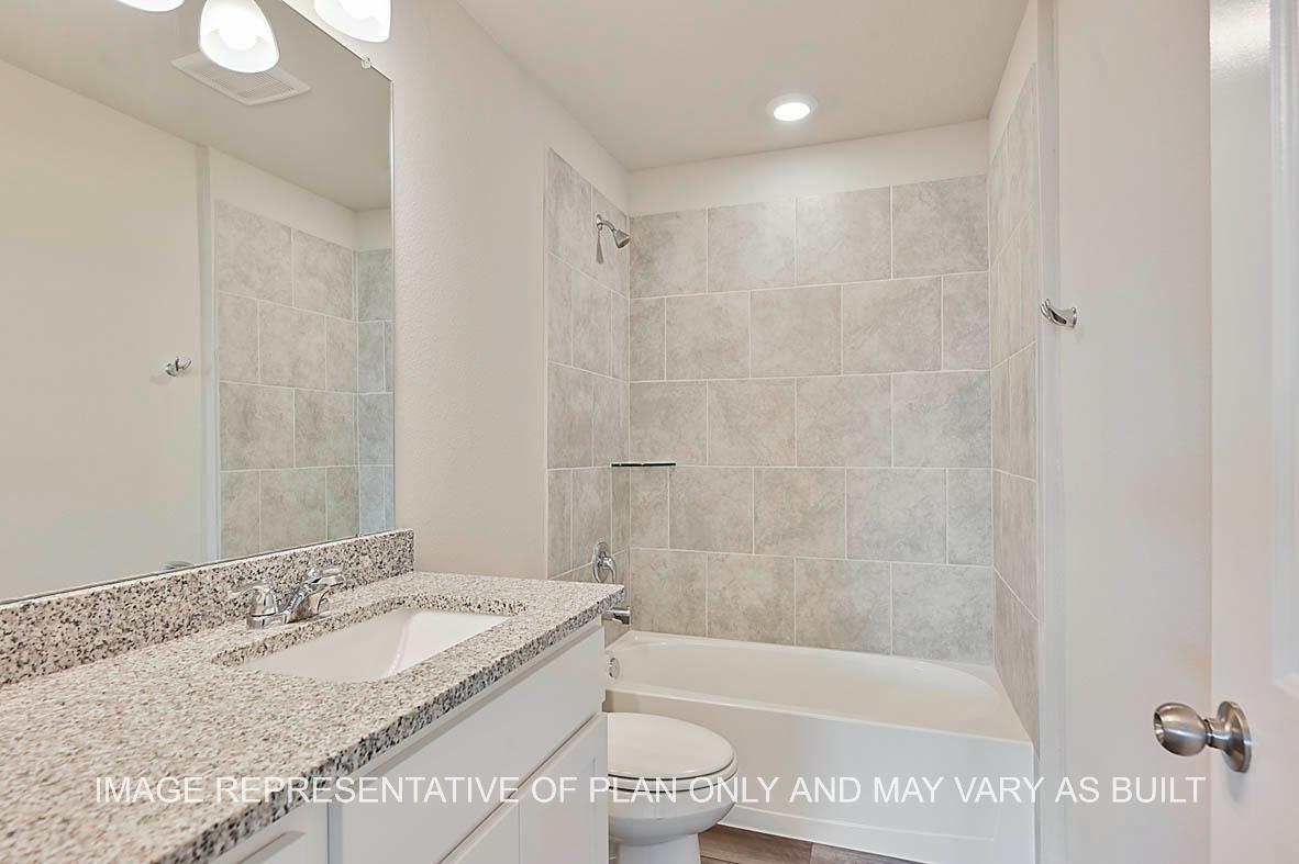 Kiawa secondary bathroom with granite countertops, white cabinetry, ceramic tile surround, and vinyl plank flooring.