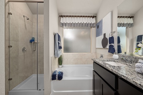 Southern Pointe model home primary bathroom with granite countertops, ceramic tile shower and tub, and shaker cabinets