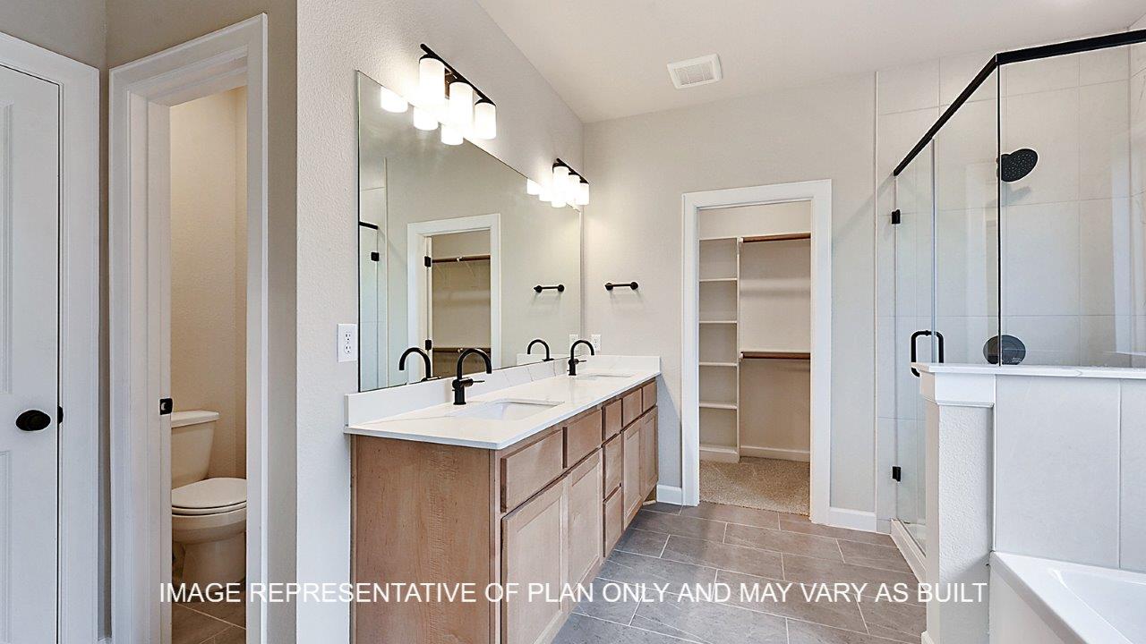 Stratford primary bathroom with tile flooring, separate tub and shower, light stained cabinets and white quartz countertops.