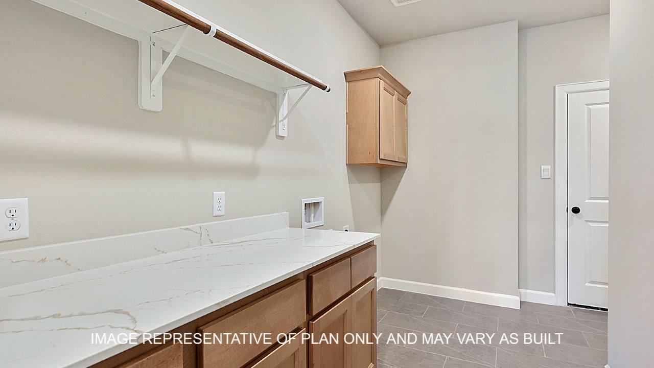 Stratford utility room with light stained cabinets, white quartz countertop with hanging rack for clothing.