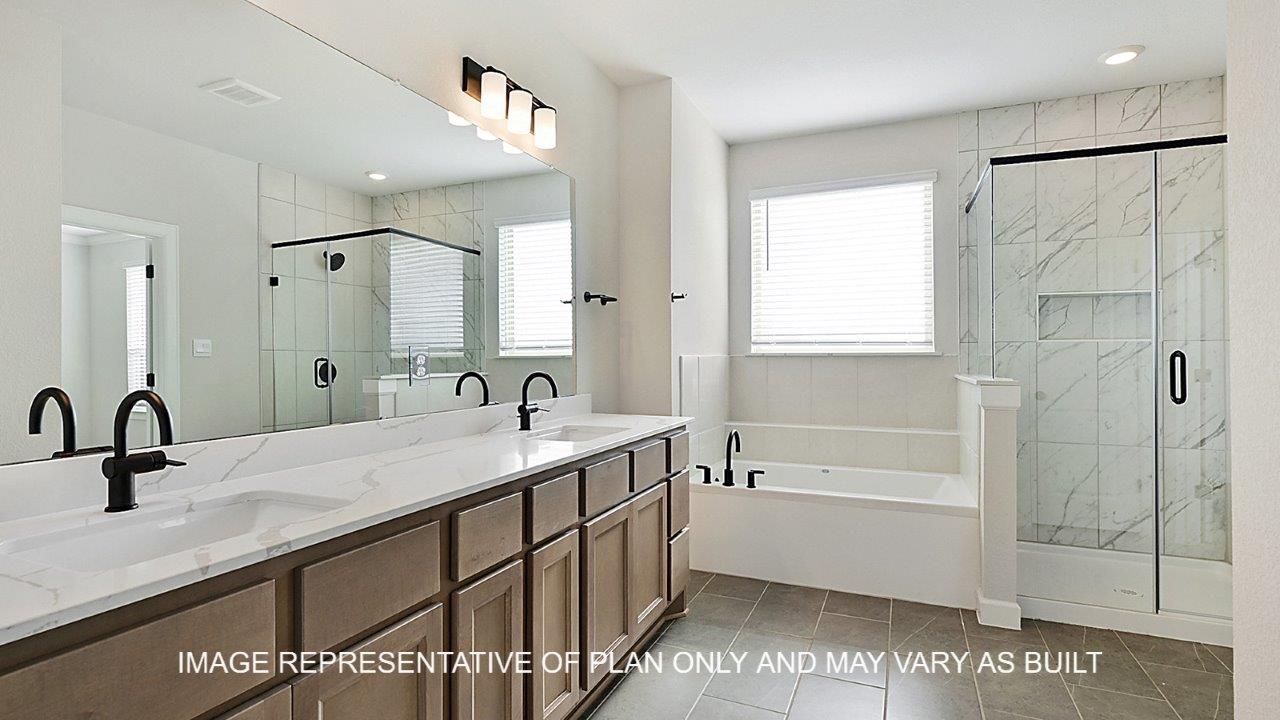 Kensington primary bathroom with tile flooring, separate tub and shower, light stained cabinets and white quartz countertops.