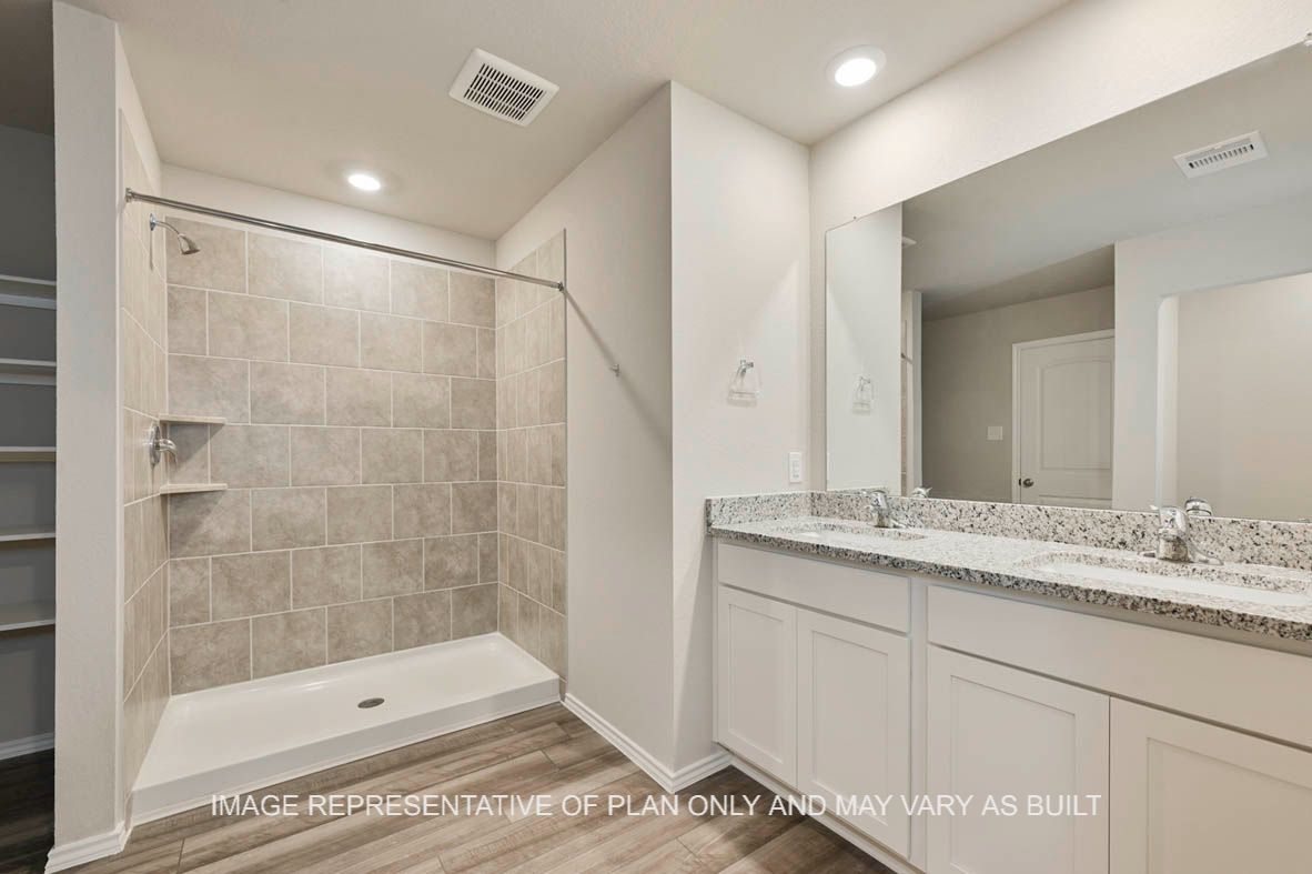 Texas Cali primary bathroom with white cabinets, granite countertops, ceramic tile shower surround and vinyl plank flooring.