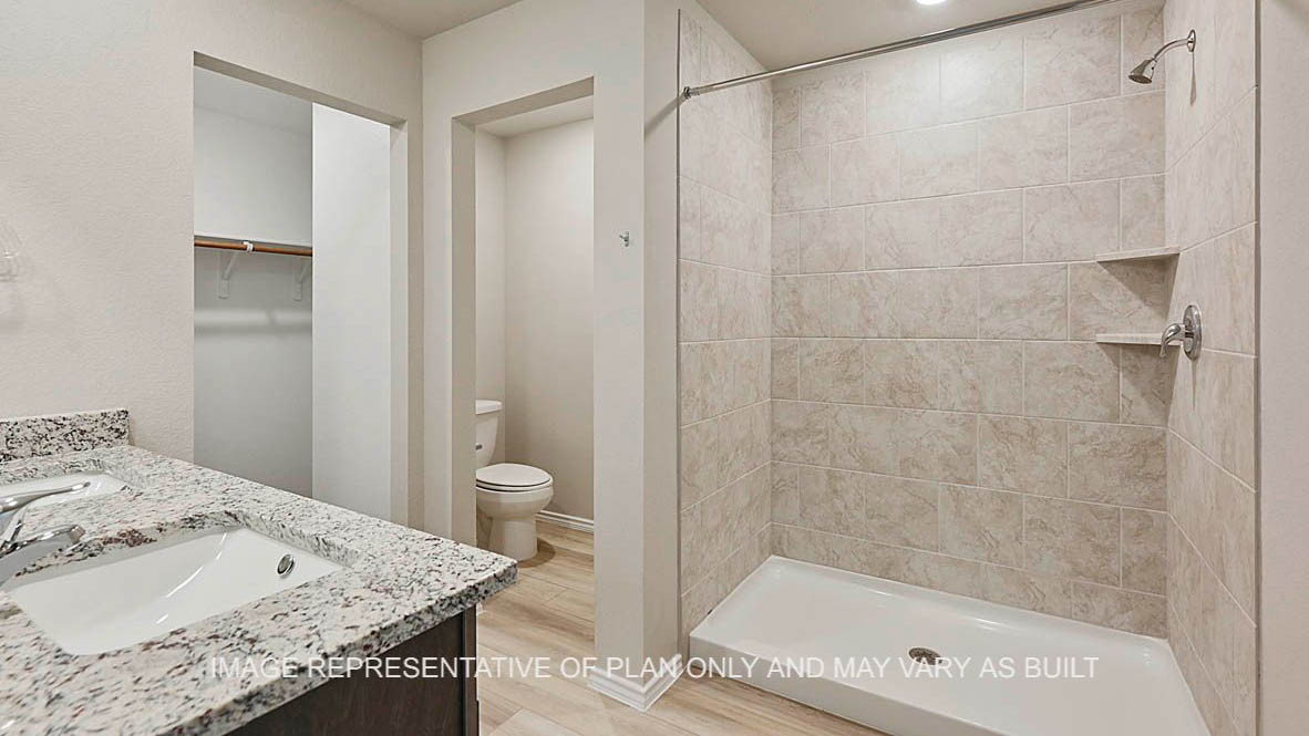 Elgin primary bathroom with dark stained cabinets, granite countertops, ceramic tile shower surround, and vinyl plank flooring.