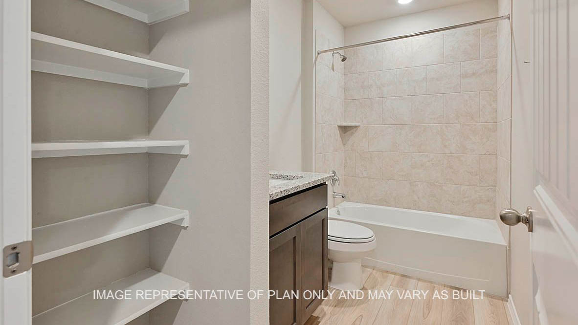 Elgin secondary bathroom with dark stained cabinetry, granite countertops, ceramic tile shower bath surround, linen shelving, and vinyl plank flooring.