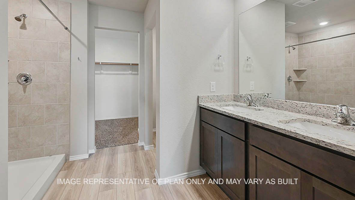 Fargo primary bathroom with dark stained cabinetry, granite countertops, ceramic tile shower surround, vinyl plank flooring and view to closet.