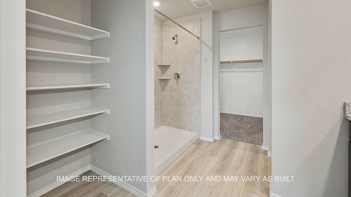 Fargo primary bathroom with dark stained cabinetry, granite countertops, ceramic tile shower surround, linen shelving, vinyl plank flooring and view to closet.