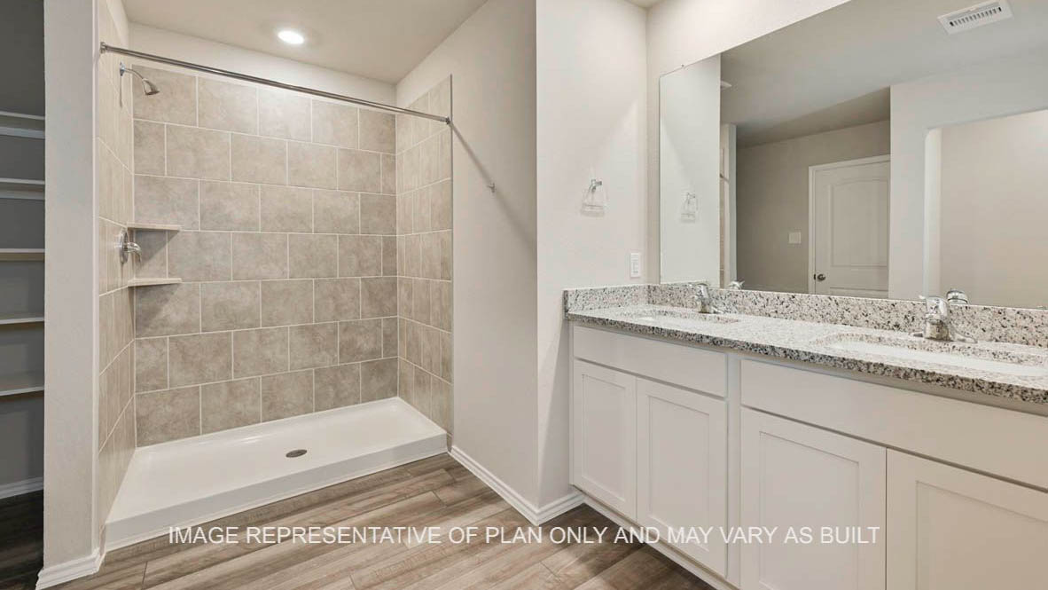 Texas Cali primary bathroom with white cabinets, granite countertops, ceramic tile shower surround and vinyl plank flooring.