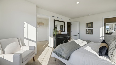 The model primary bedroom is decorated with an armchair and dresser