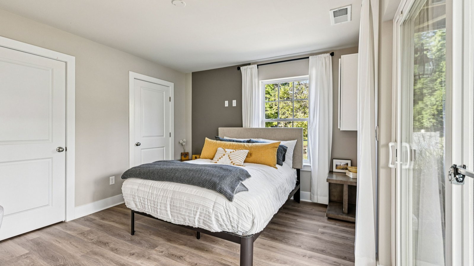 Bedroom — queen bed with yellow pillows, gray accent wall, and two side windows.