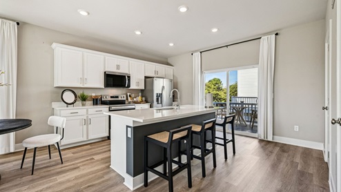 Kitchen — island with three stools, white cabinets, and sliding door to deck.