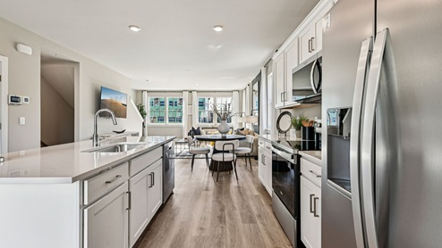 Kitchen to living — stainless appliances, long island, and wall-mounted TV in open layout.