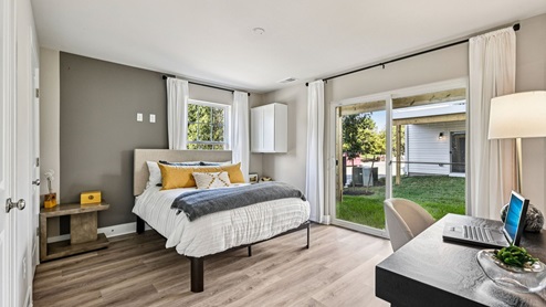Bedroom — queen bed with gray accent wall, desk by slider doors, and backyard view.