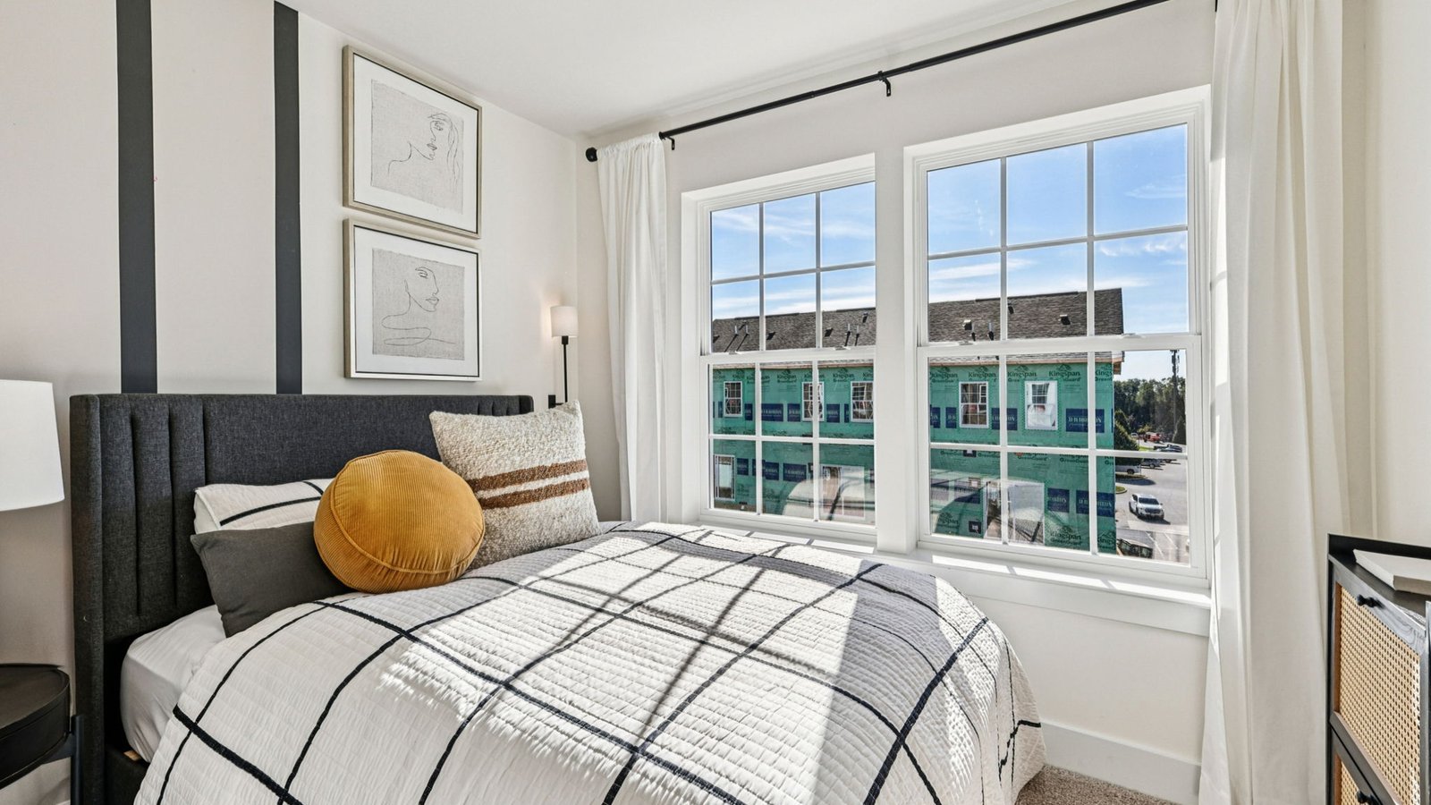 Bedroom — queen bed with striped bedding beside triple windows overlooking construction across street.