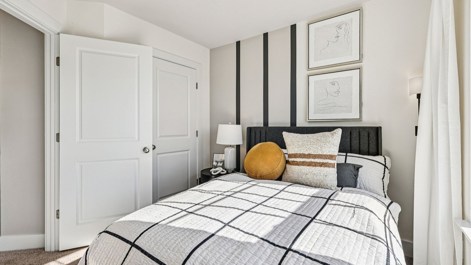 Bedroom corner — bed with black headboard, stacked line art, and round gold accent pillow.
