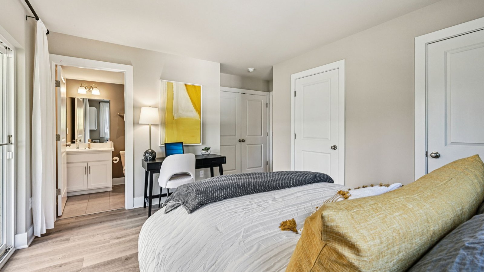 Bedroom and ensuite — view from bed to vanity, desk nook, and multiple doors.