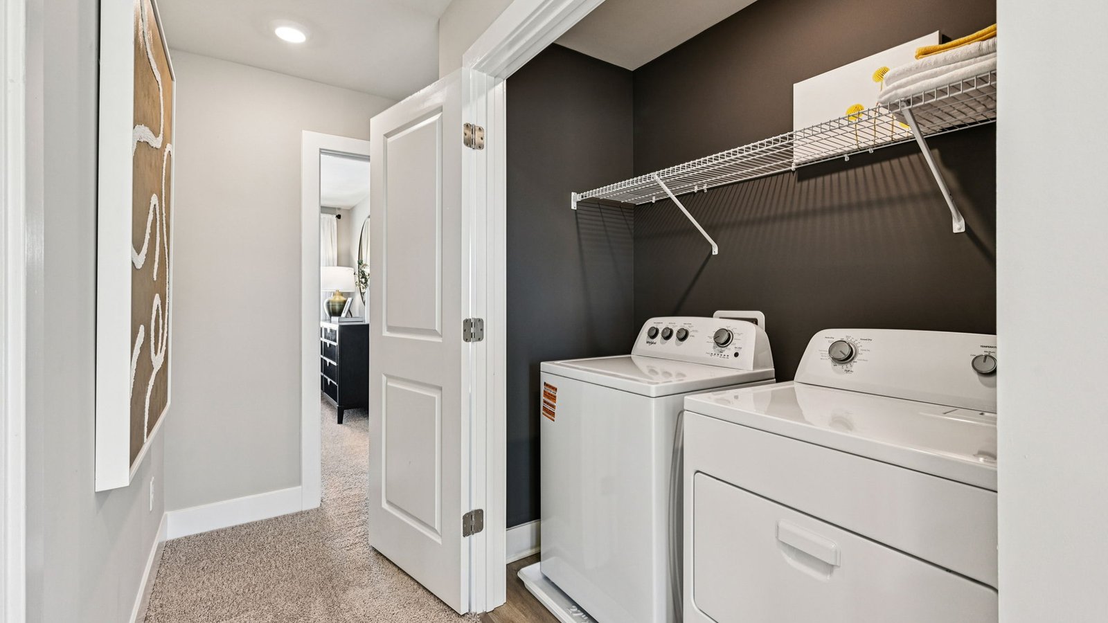 Laundry closet from hall — washer and dryer under long wire shelf.