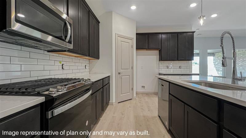 Kitchen features an island with a sink, white quartz countertops, ebony colored shaker-style cabinets, white subway tile backsplash, and stainless steel appliances.