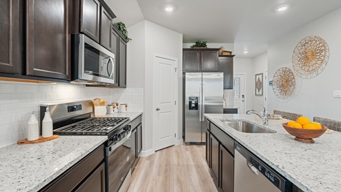 A clean kitchen with dark shaker style cabinets, modern finishes and stainless-steel appliances with a hallway leading to the front entryway.