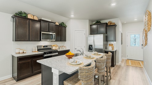 A warm kitchen with dark shaker cabinets, a large center island with three woven barstools, and stainless-steel appliances.