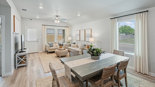 A view from the dining room into the living room and backyard, with and six woven dining chairs surrounding a large gray dining table.