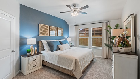 A calming primary bedroom with one blue accent wall, a large bed with a woven bed frame, two white bedside tables with a large matching dresser, and two windows with light curtains.