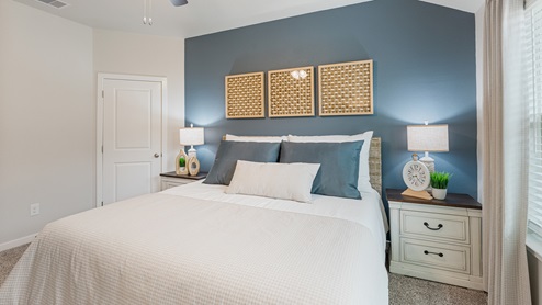 A calming primary bedroom with one blue accent wall, a large bed with a woven bed frame, two white bedside tables with farmhouse decor, and a door to the walk-in closet.