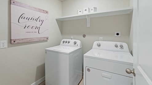 A clean laundry room with farmhouse decor, and a washer and dryer with shelving above.