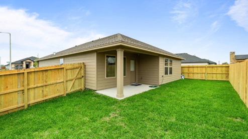 A spacious backyard with green grass and wooden fencing surrounding a single-story home with tan siding.