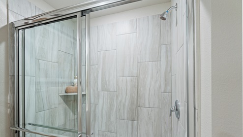 Spacious walk in shower with built in shelving and light gray tiles.