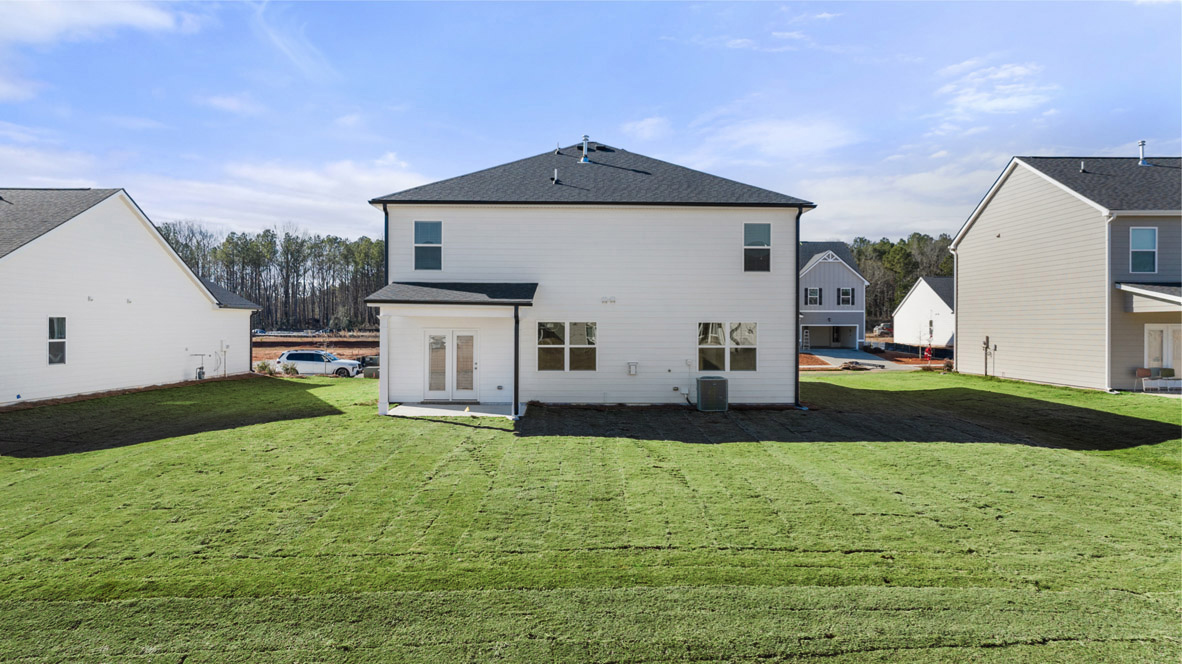 Two story home from behind with lush lawn and back patio.