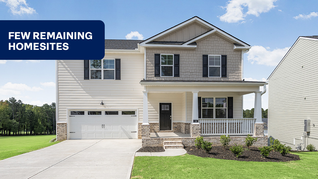 Two story home with covered front porch and two car garage and flag saying "FEW REMAINING HOMESITES"
