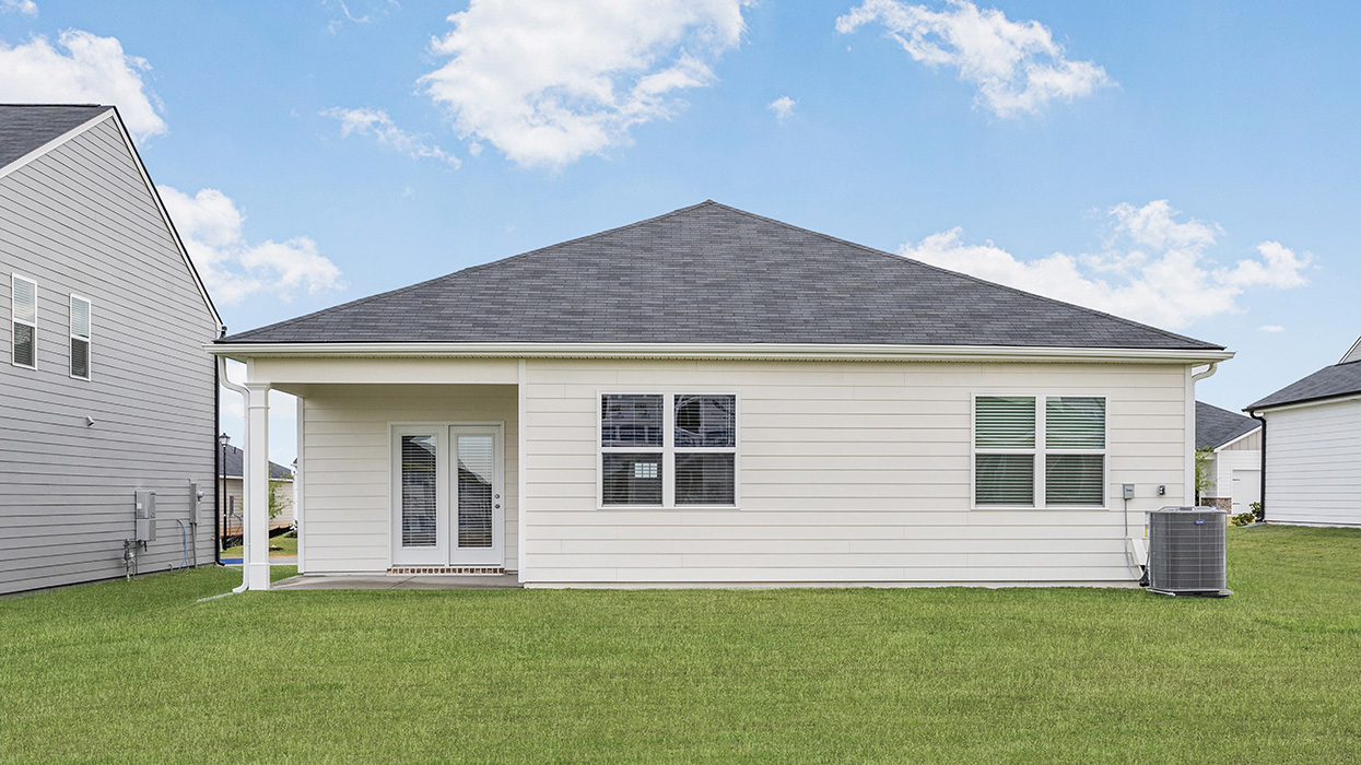 Rear of single-family ranch home in cream with covered back porch and lush lawn