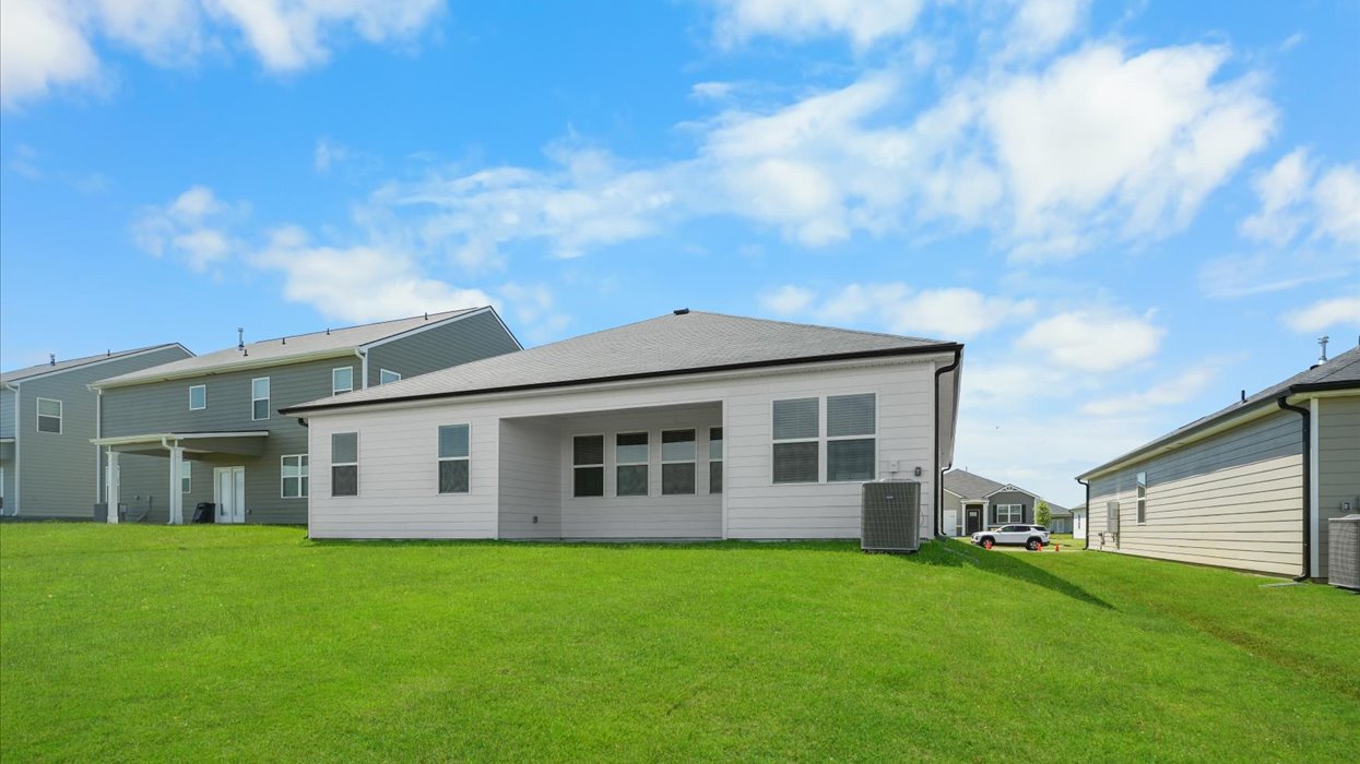 Rear of single story white ranch home with covered back porch and lush lawn