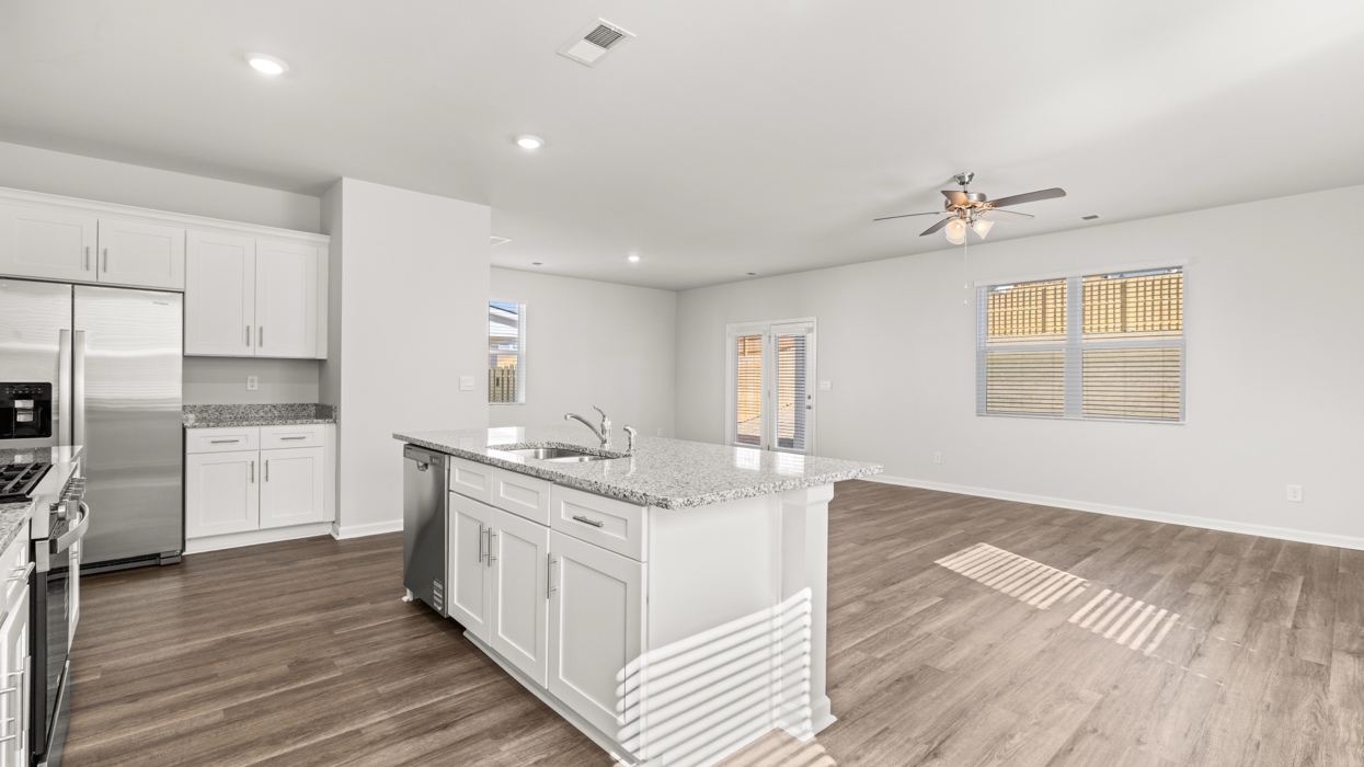 Bright modern kitchen with granite counters, stainless steel appliances, and large center island opening to living and dining space.